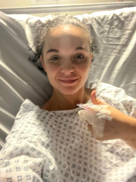 A person in a hospital gown giving a thumbs up.