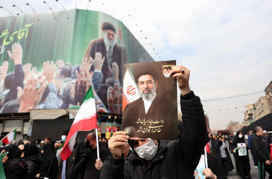 A person holds up a portrait of military official Sayyed Reza Mousavi at a funeral with a large billboard of Iran's Supreme Leader Ayatollah Ali Khamenei in the background.
