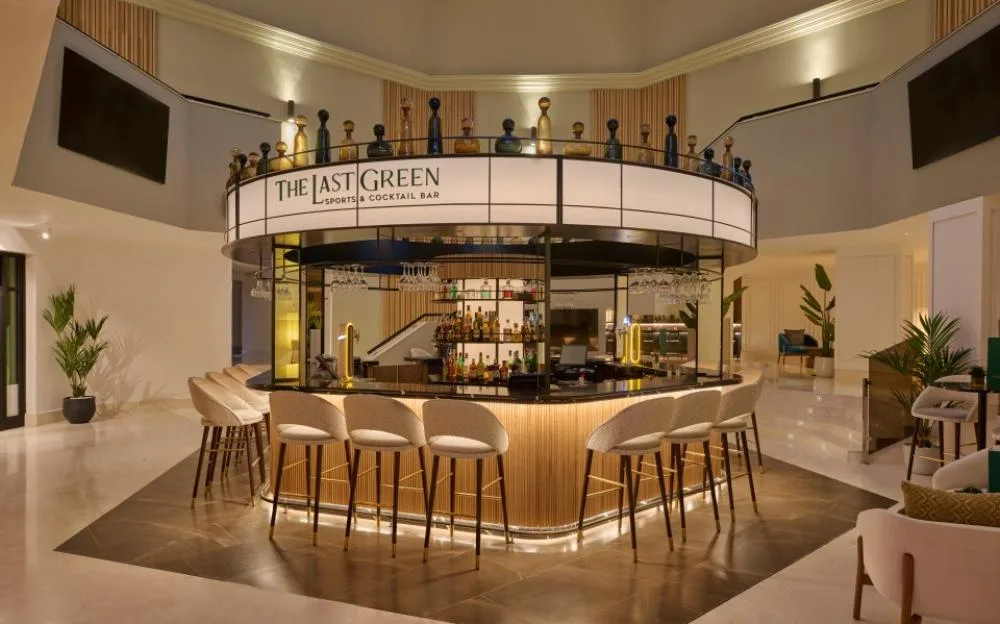 The Last Green sports and cocktail bar, featuring a circular counter with white bar stools and decorative bottles along the top rim.