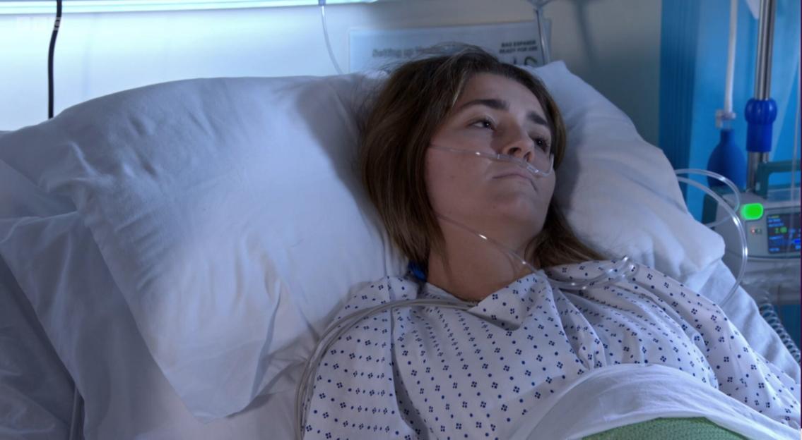 A woman in a hospital gown and oxygen cannula lies in a hospital bed.