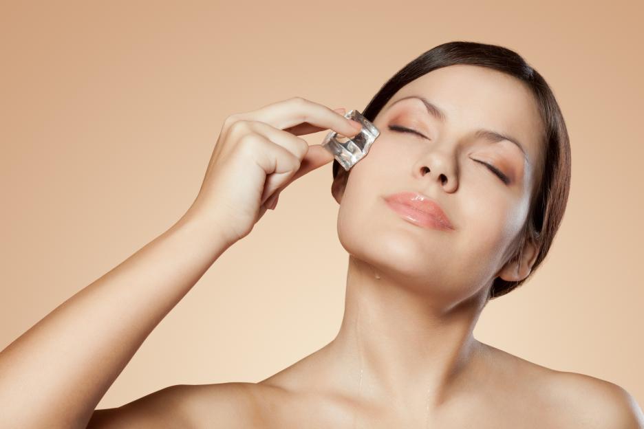 Brunette woman holding an ice cube to her face for skin care.