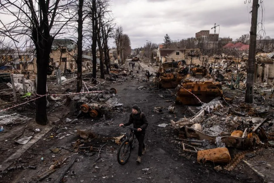 A man pushes his bike through debris and destroyed military vehicles on a street in Bucha, Ukraine.