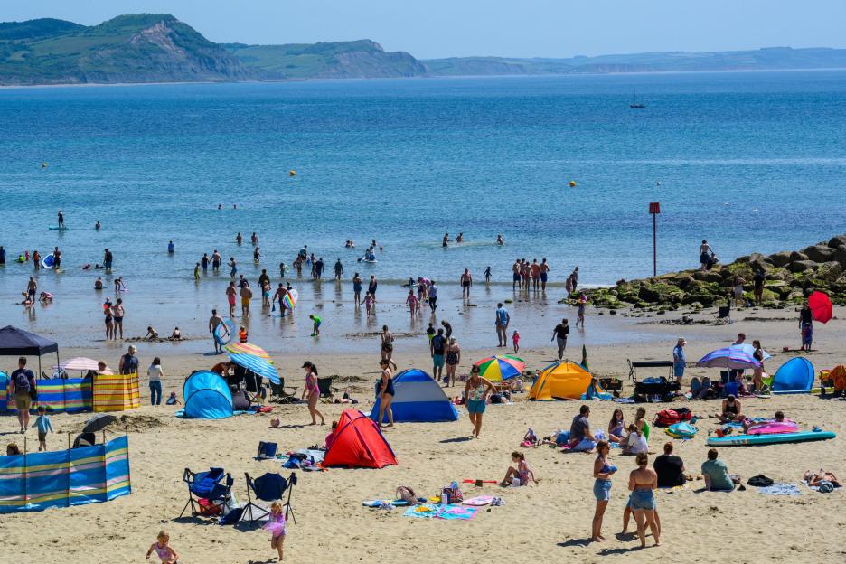 People enjoying a sunny day at the beach, with many swimming in the sea and others relaxing on the sand.