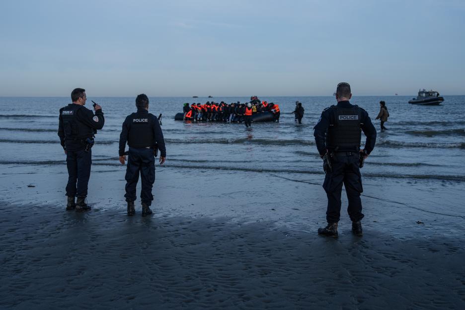 Police officers observe migrants boarding a dinghy to cross the English Channel.