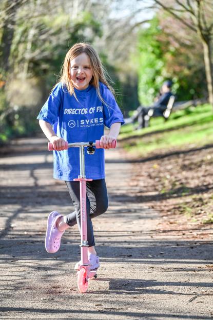 Matilda, a 'Director of Fun' for Sykes Holiday Cottages, rides a pink scooter.