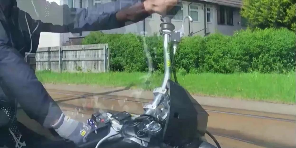 A person on an e-bike, viewed from the perspective of the bike's handlebars, travels down a road alongside tram tracks.