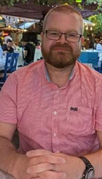 Headshot of a man with a beard and glasses, wearing a red checkered shirt.