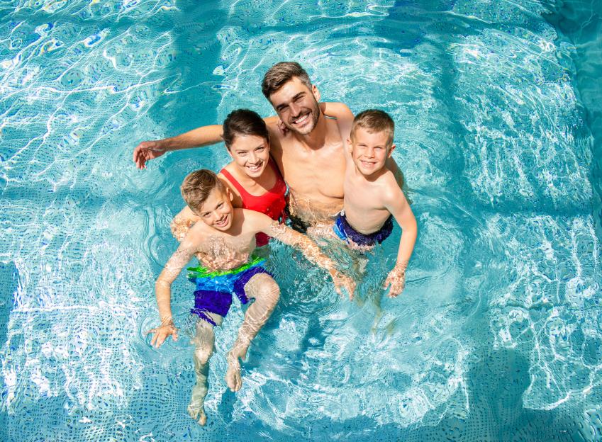 Top-view of a smiling family of four in a swimming pool.