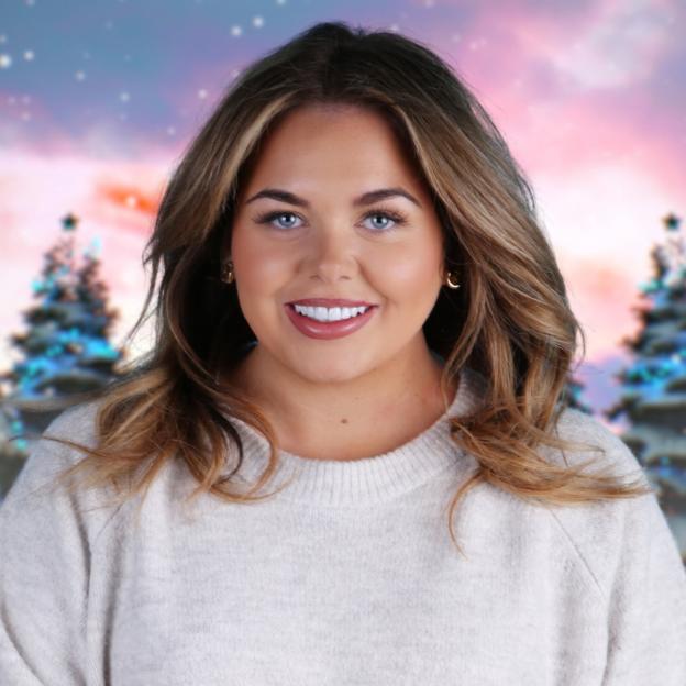 Scarlett Moffatt smiles with a snowy, pastel pink, and purple background with two blurry Christmas trees.