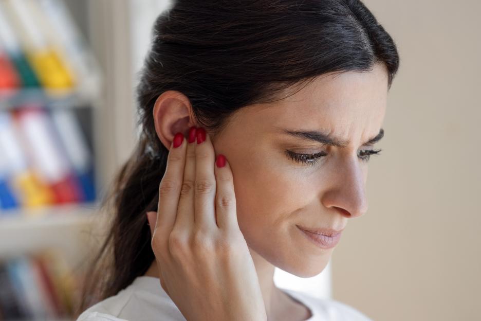 A woman grimacing and holding her ear due to ear pain.