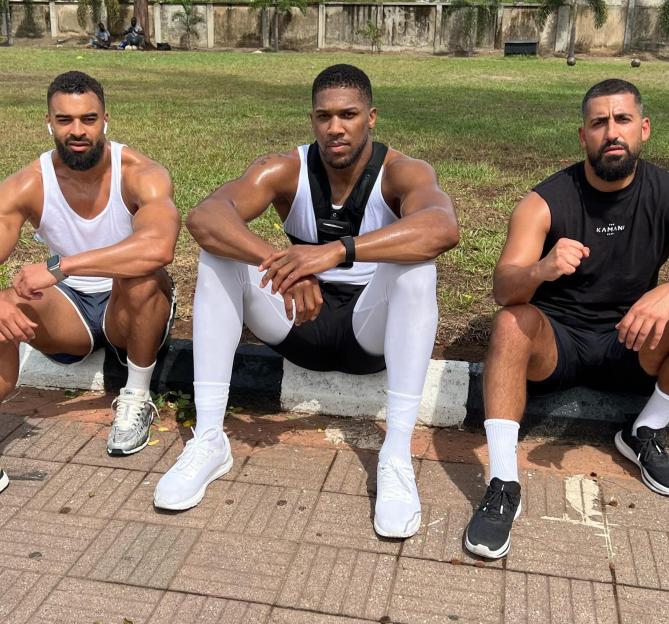 Anthony Joshua and two friends sitting on a curb after a workout.