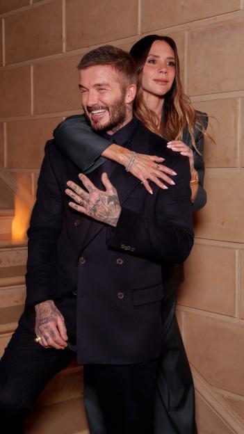 David Beckham embracing Victoria Beckham, who stands behind him with her arms around his shoulders.