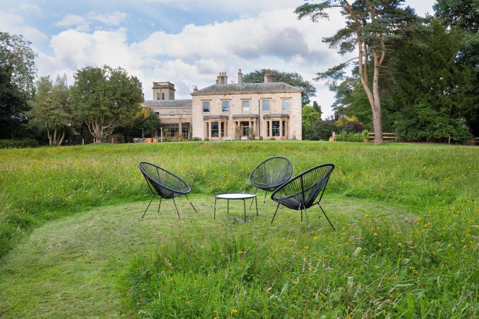 A stone country house in Cumbria with a tower, surrounded by green lawns and trees.