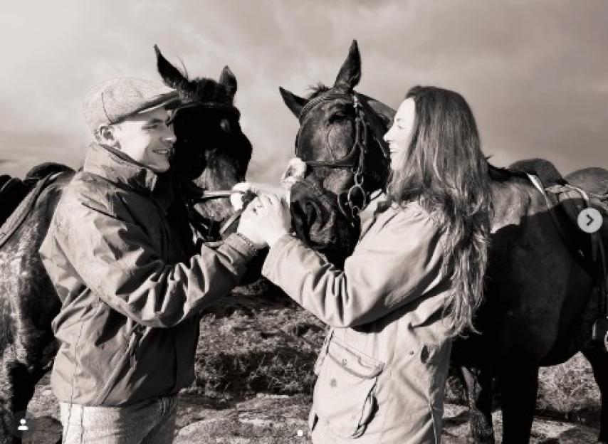 A man in a cap and a woman with long hair holding the bridle of a horse.