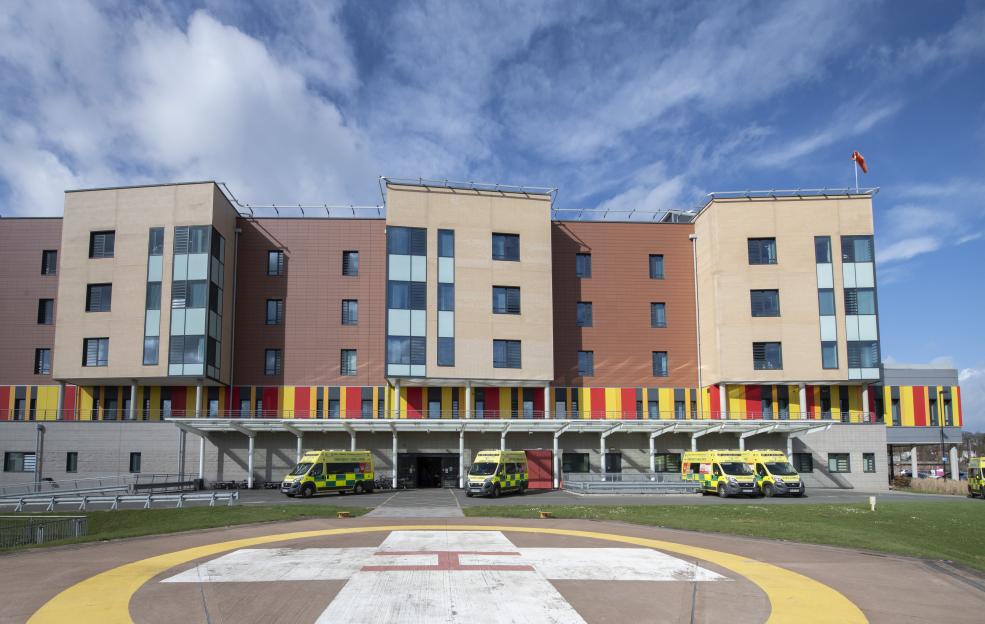 The exterior of Royal Stoke University Hospital's Accident and Emergency department, with ambulances parked outside and a helipad in the foreground.