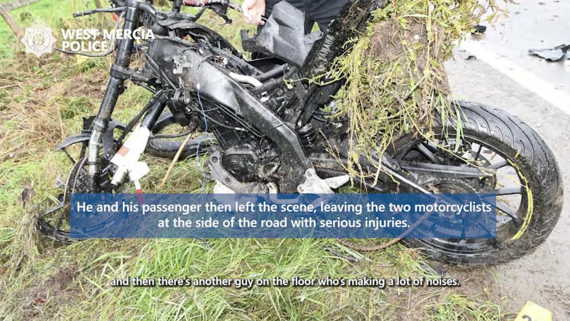 A damaged motorcycle partially covered in grass lies on the side of a road after a collision.