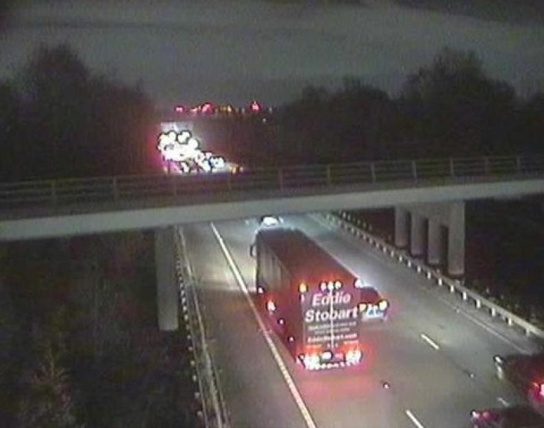 Overhead view of halted traffic on a highway at night, with emergency vehicle lights visible in the distance.