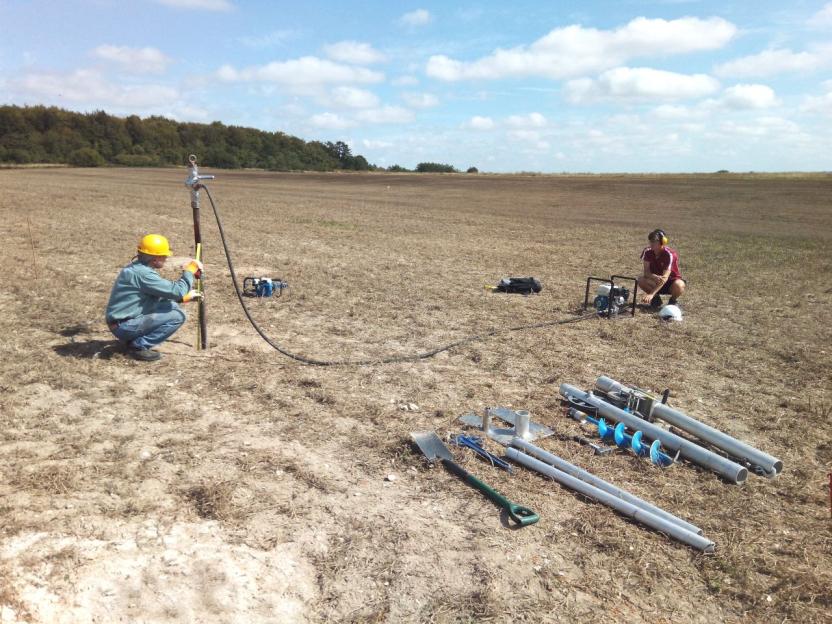 Two people conducting field tests in a dry, open field with specialized equipment for soil sampling.