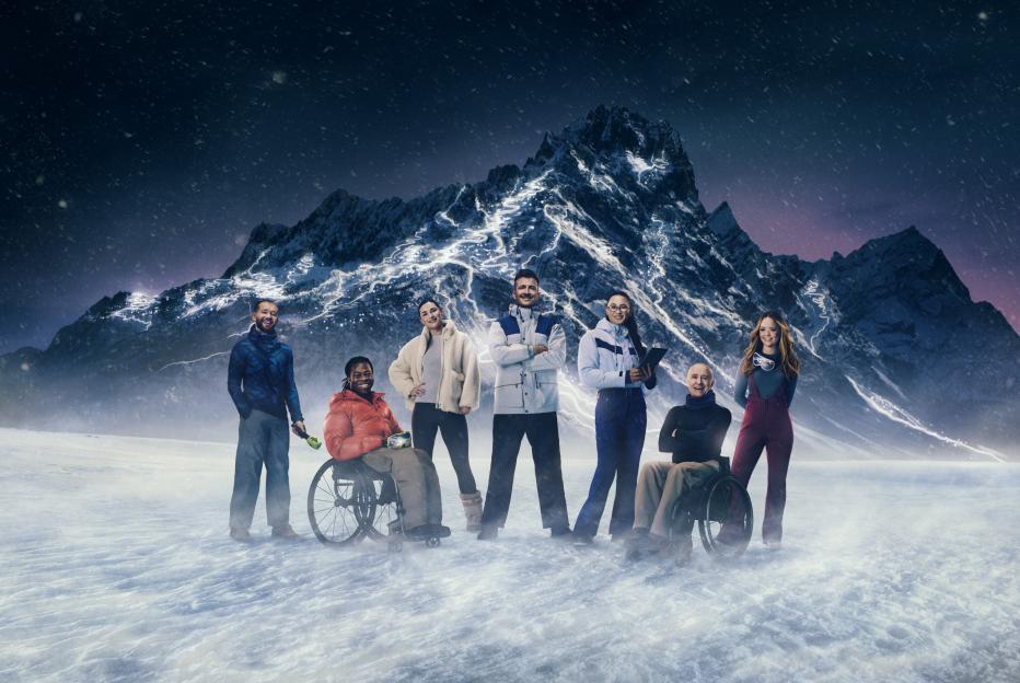 Seven people posing in front of a snowy mountain landscape at night, with two in wheelchairs.