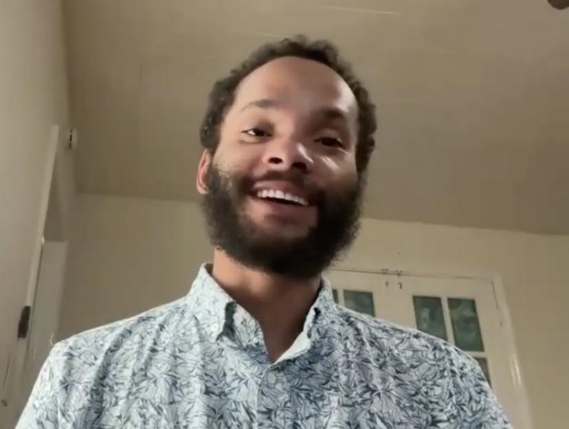 Gene Long, a man with a beard and curly hair, smiles at the camera in a video still.
