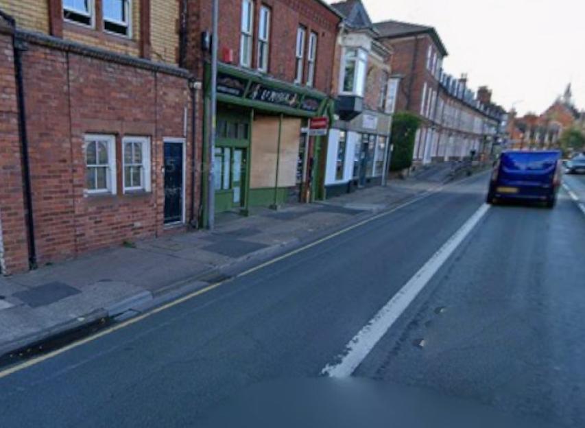 A street view of a blue van driving past buildings with storefronts on the left.