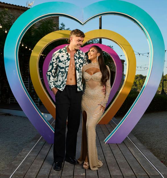 Shakira Khan and Harry Cooksley standing in front of a colorful heart-shaped 'Love Island' sign.