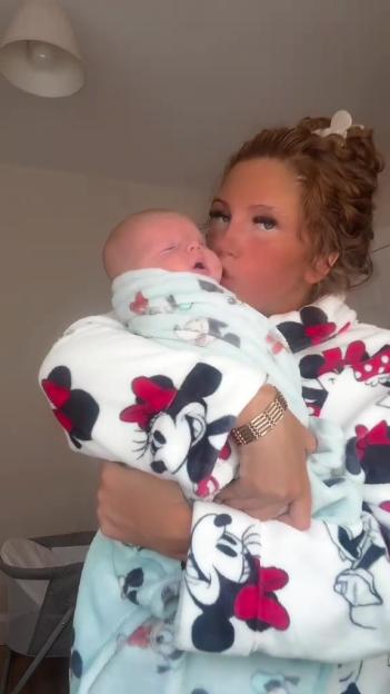 A person in a Minnie Mouse bathrobe holding a baby swaddled in a Mickey Mouse blanket.