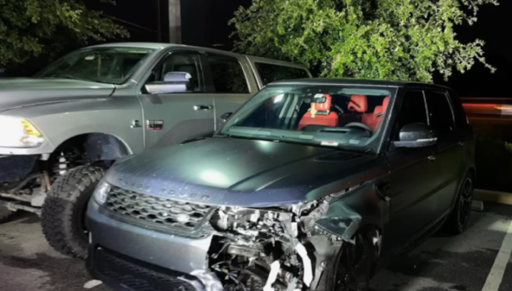 A black Range Rover with significant front-end damage parked next to a lifted gray pickup truck.