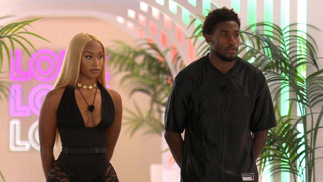 Two "Love Island" contestants, a woman with long blonde hair and a man in a black shirt, stand next to each other.