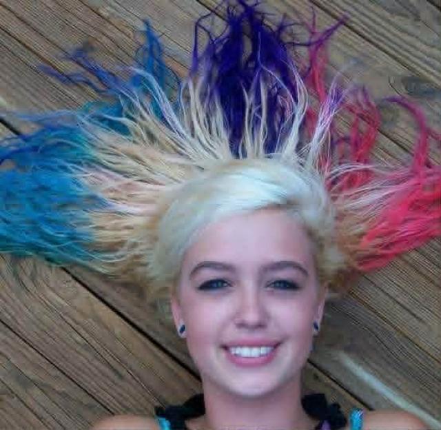 Smiling young woman, Katlyn Sale, with blonde hair dyed blue, purple, and pink, fanned out on a wooden surface.