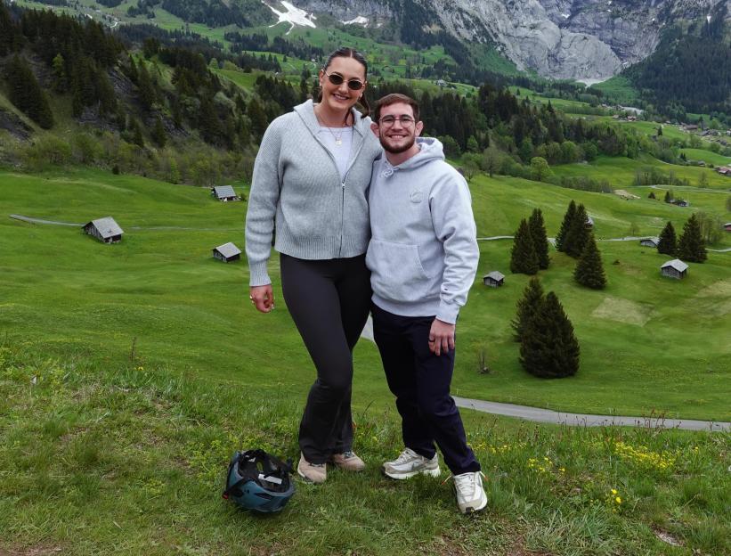 Lucas Byrd and Ellie Holzman stand in a mountainous green landscape.