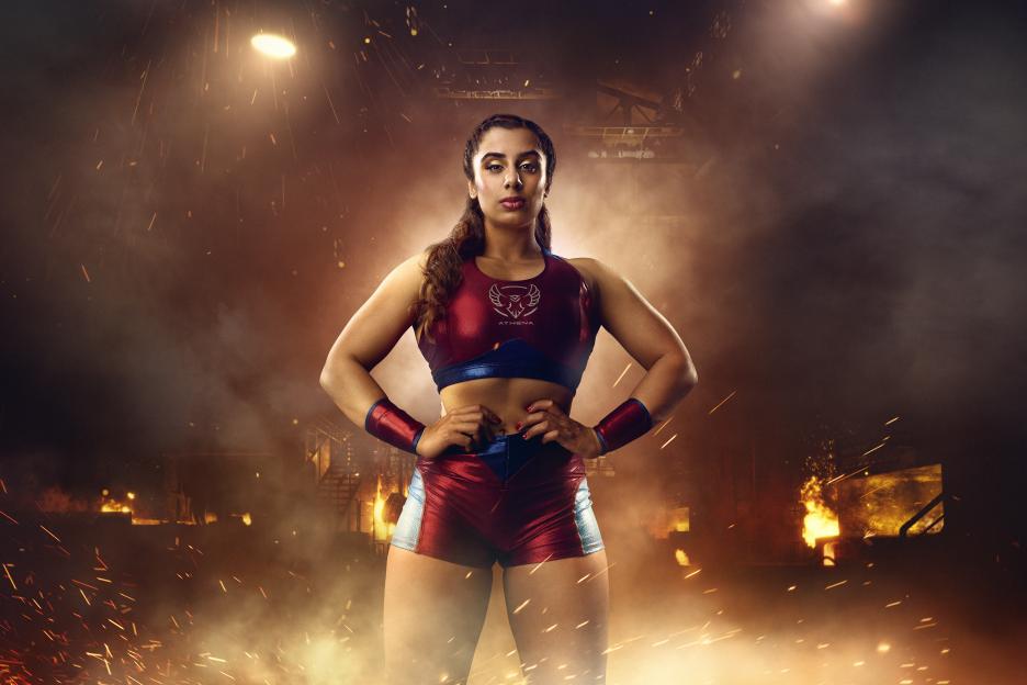 Athena from Gladiators Season 2, a woman with braided hair, in a red and blue sports outfit with "ATHENA" written on her top.