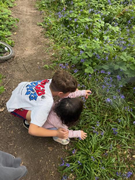 Two children looking at blue flowers by a dirt path.