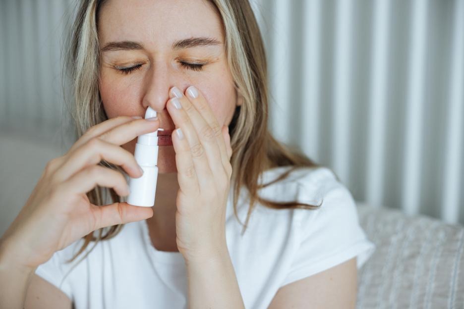 Woman in a white shirt with closed eyes using a nasal spray.