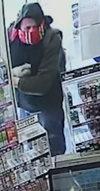 CCTV image of one of two men who robbed a shop at gunpoint, wearing a hooded jacket and a red and white striped mask.
