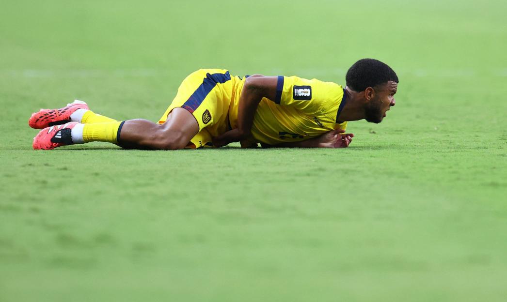 A soccer player in a yellow and blue uniform lies face down on the grass.