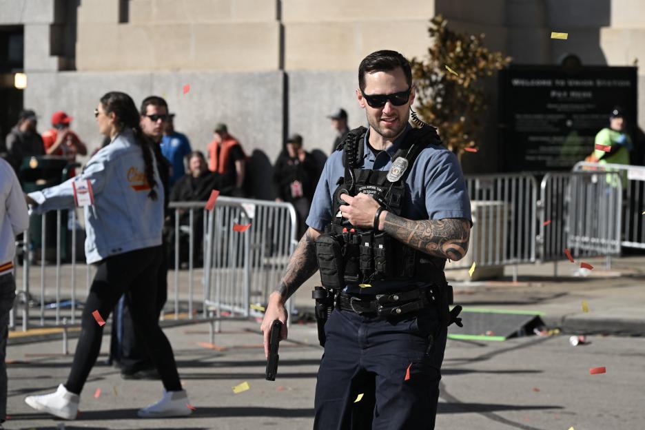 A police officer with a gun in hand walks with confetti falling around him after shots were fired near the Kansas City Chiefs' Super Bowl LVIII victory parade.