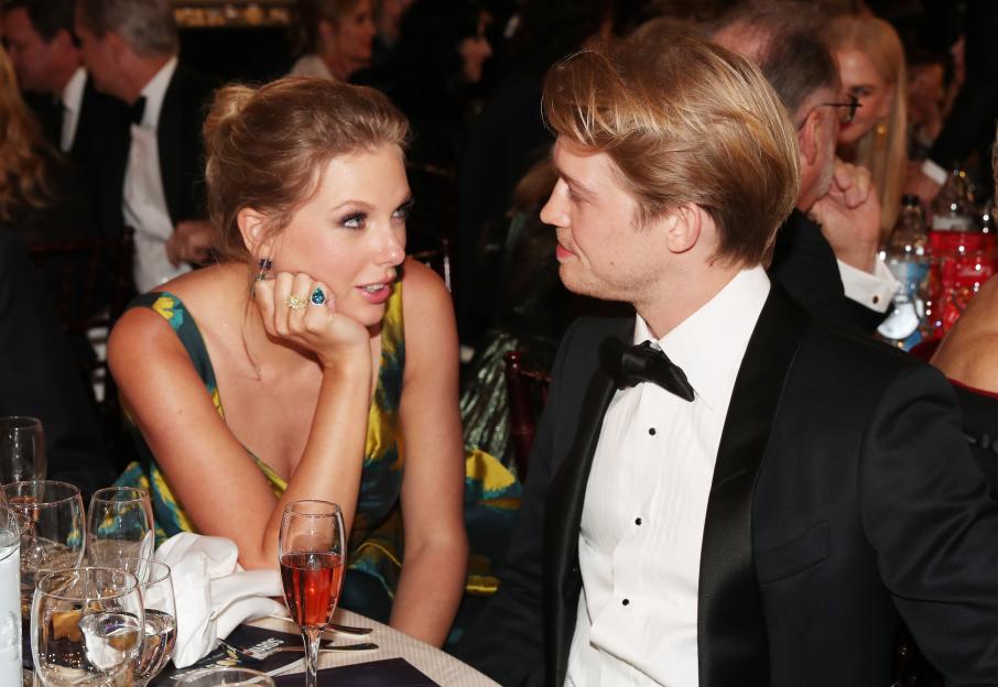 Taylor Swift in a colorful dress and Joe Alwyn in a tuxedo conversing at the Golden Globe Awards.