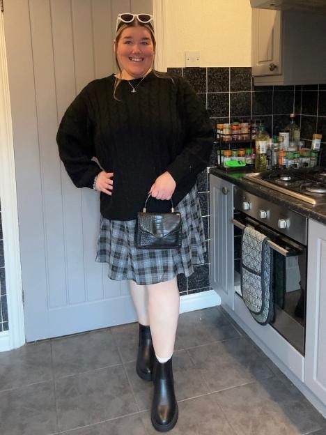 Becki Jones in a black sweater and plaid skirt holding a small black purse.