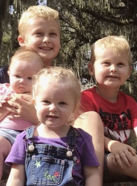 Four young children, three boys and one girl, smiling at the camera.