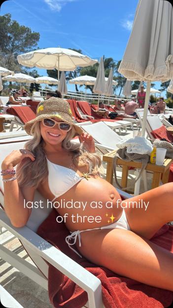 A pregnant woman in a white bikini and straw hat smiles while relaxing on a sun lounger.