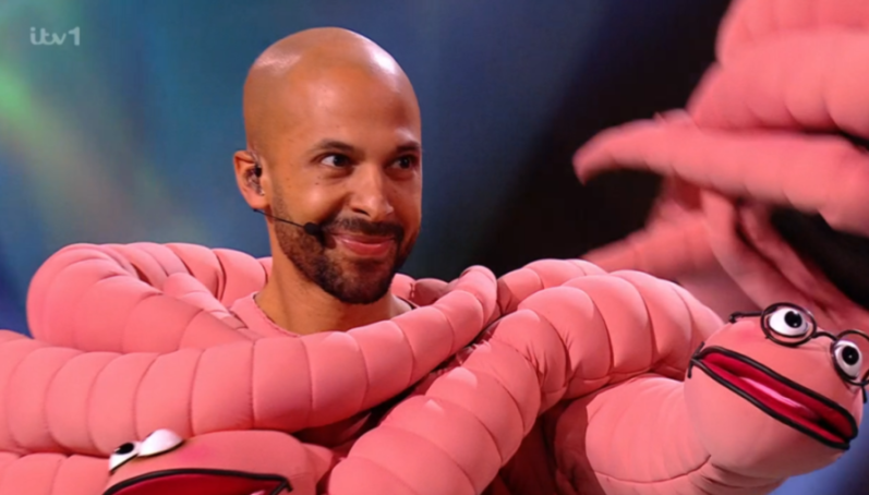 Bald man in a pink worm costume with worm puppets.