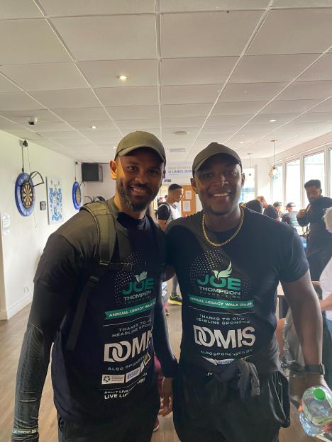 Two men wearing black t-shirts and caps, smiling.