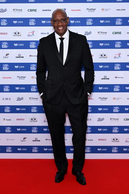 Shaun Wallace in a black suit with a black tie on a red carpet at the British Diversity Awards.