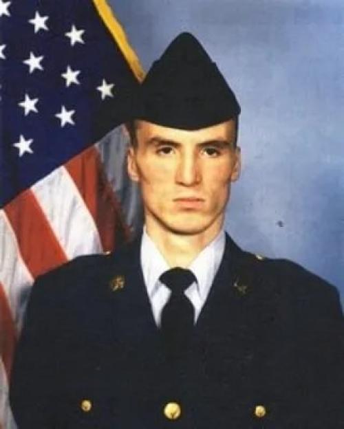 Young man in a military uniform standing in front of an American flag.