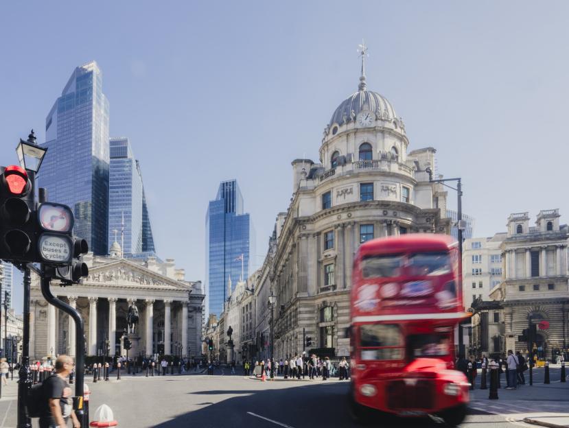 Red double-decker bus blurring past historic buildings and modern skyscrapers in London.