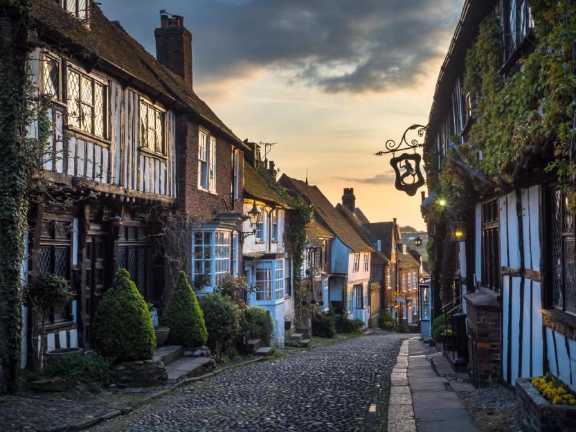 Mermaid Street in Rye, East Sussex, features historic timber-framed houses lining a cobbled street at dusk.