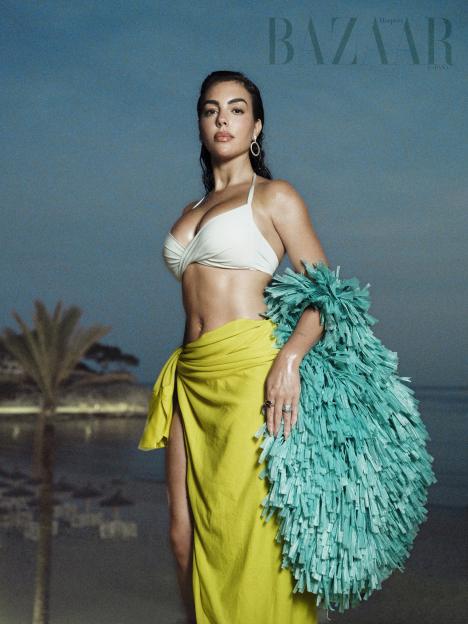 Woman wearing a white bikini top, yellow sarong, and turquoise fringe garment.