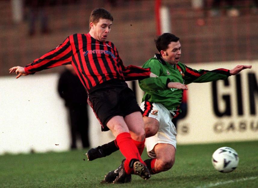 Two soccer players challenge for the ball on a grassy field.