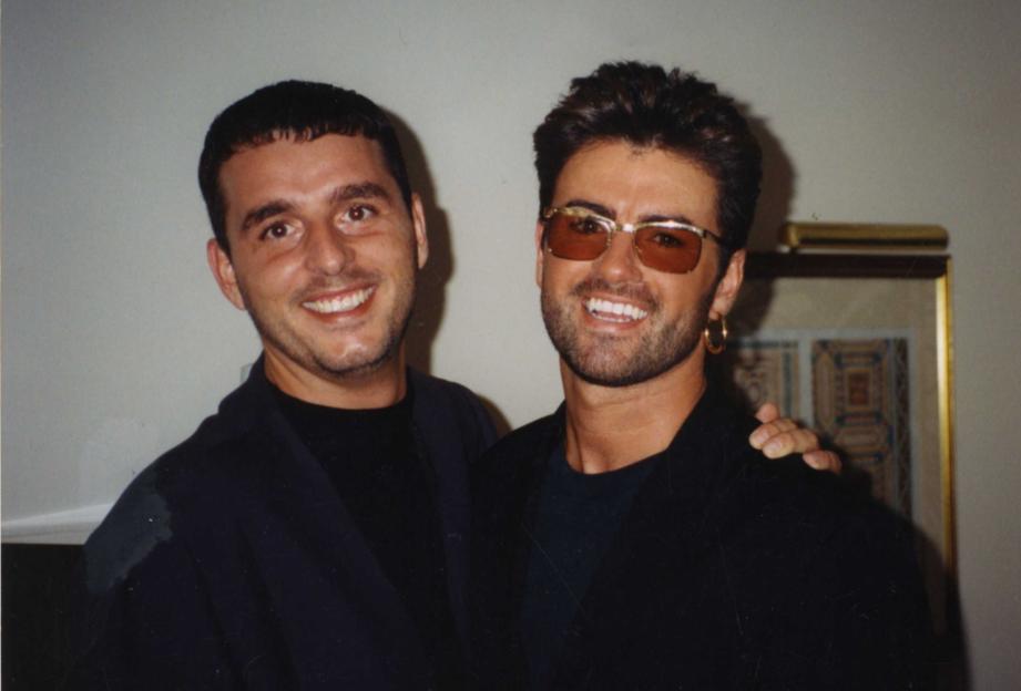 Andros Georgiou and George Michael smiling with an arm around each other.